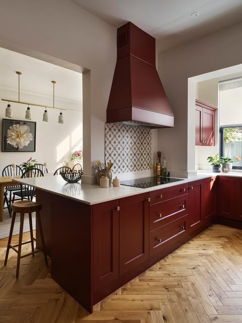 Hand-painted kitchen in deep oxblood red with a cream stone worktop and herringbone oak floor